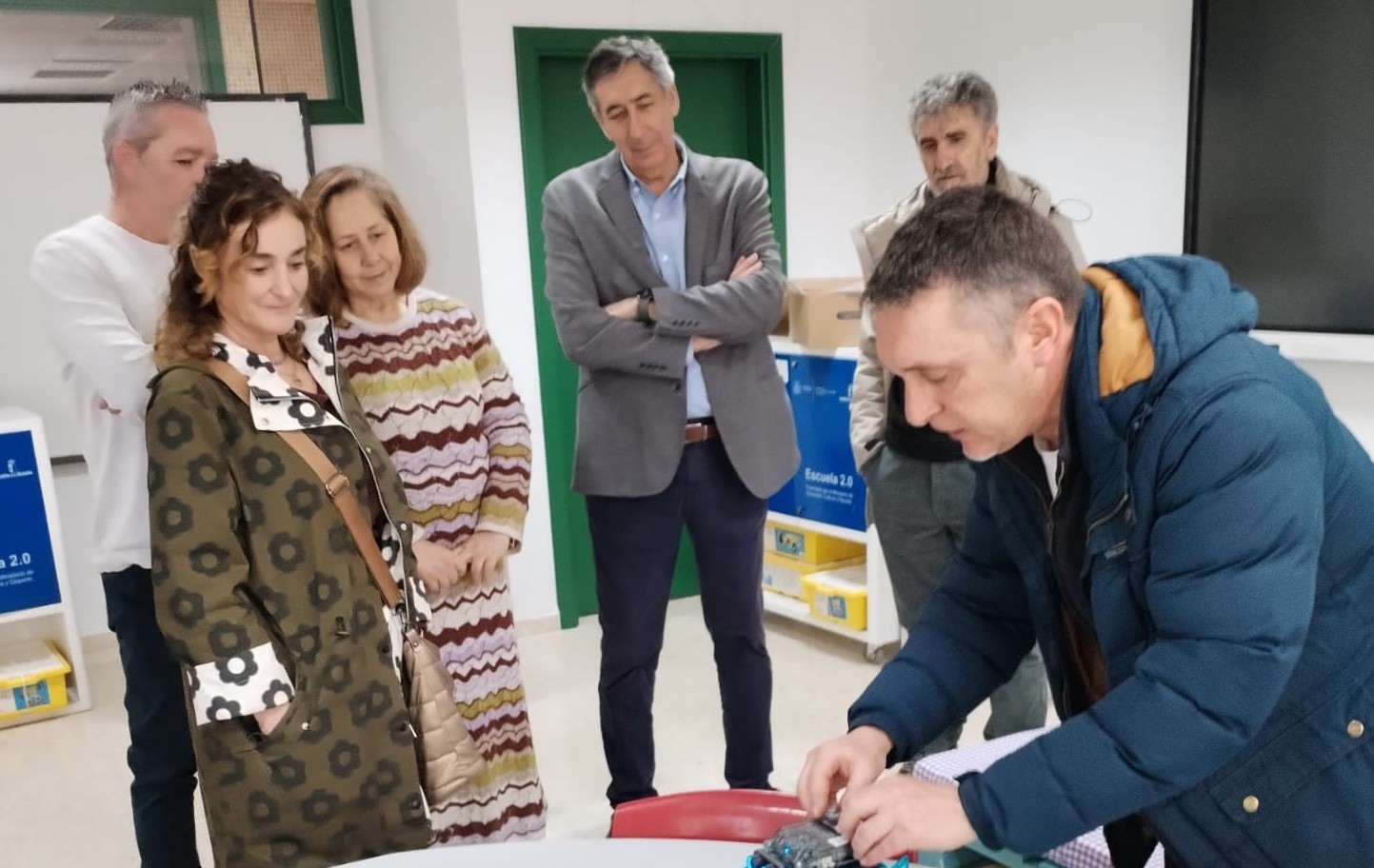 Un grupo de personas observa una demostración de robótica educativa mientras un docente manipula un pequeño robot sobre una mesa con materiales tecno