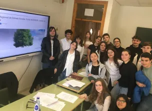 Grupo de estudiantes y profesorado en un aula durante una sesión de la Liga Regional de Debate Escolar, posando junto a mesas de trabajo y una pantal