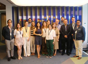 Fotografía grupal de los participantes del proyecto posando frente a un panel con banderas de países de la Unión Europea. Los asistentes aparecen de 